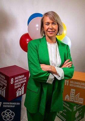 Emelie Holmlund står med grönkavaj i ett rum med lådor och ballonger bakom sig.