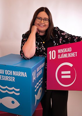 Erika Olofsson håller i en rosa låda och en blå låda med texterna "Minskad ojämlikhet" och "Hav och marina resurser".