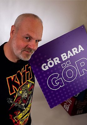 Per Persson har en t-shirt med bandet Kizz tryckt på och håller i en skylt med texten "Gör bara gör".